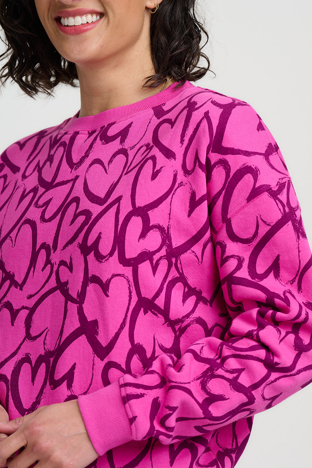Person wearing a pink sweatshirt with black heart patterns on a plain background