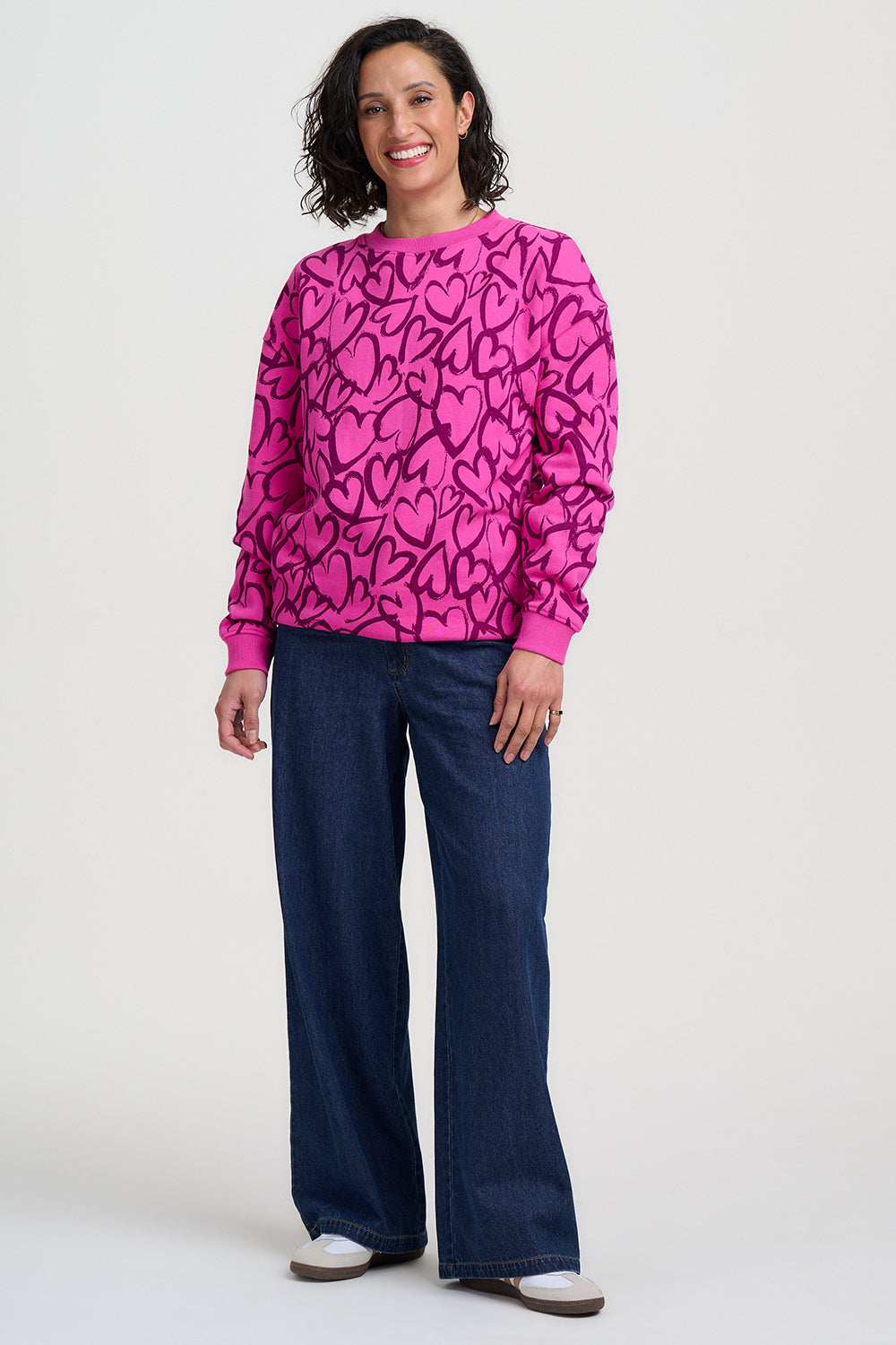 Woman wearing a pink patterned top and blue jeans on a white background
