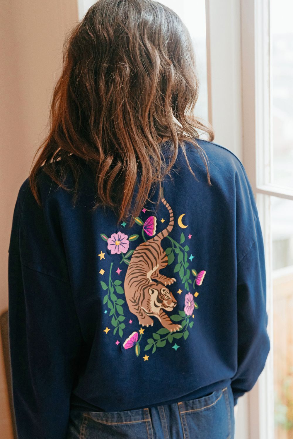 Person wearing a navy blue sweatshirt with a tiger and floral design on the back.