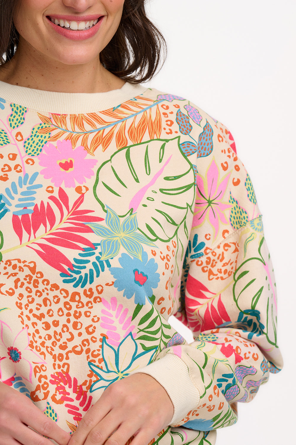 A woman wearing an oversized sweatshirt with a colourful tropical leaf and flower print on an off-white base.