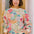 Woman wearing a colorful floral-patterned sweater standing against a wooden door.