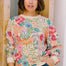 Woman wearing a colorful floral-patterned sweater standing against a wooden door.