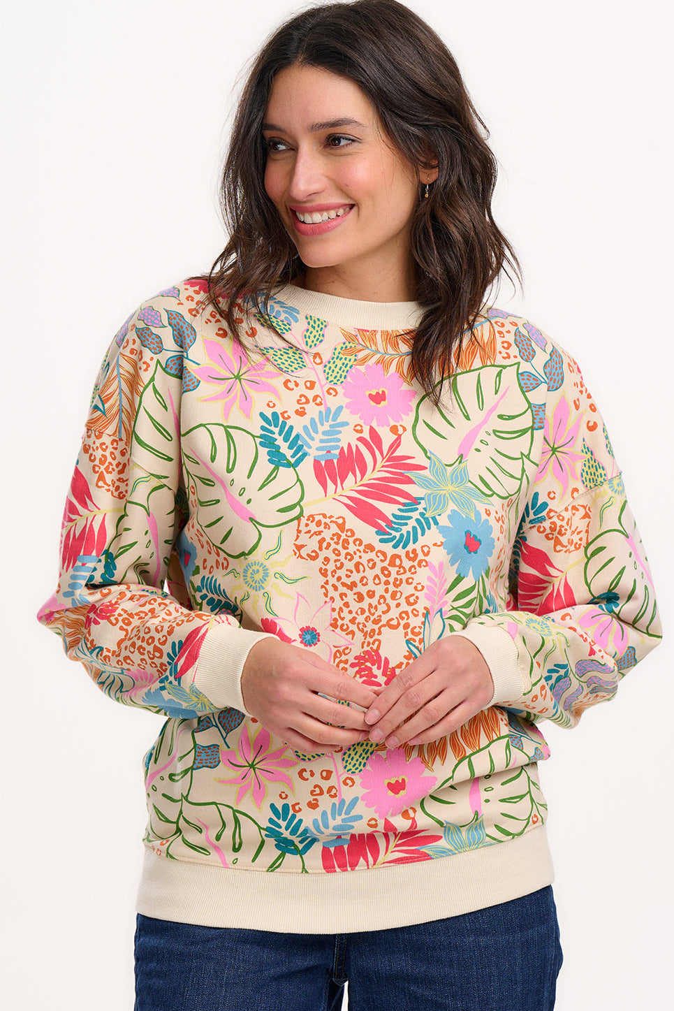 A woman wearing an oversized sweatshirt with a colourful tropical leaf and flower print on an off-white base.