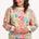 A woman wearing an oversized sweatshirt with a colourful tropical leaf and flower print on an off-white base.
