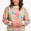 A woman wearing an oversized sweatshirt with a colourful tropical leaf and flower print on an off-white base.