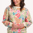 A woman wearing an oversized sweatshirt with a colourful tropical leaf and flower print on an off-white base.