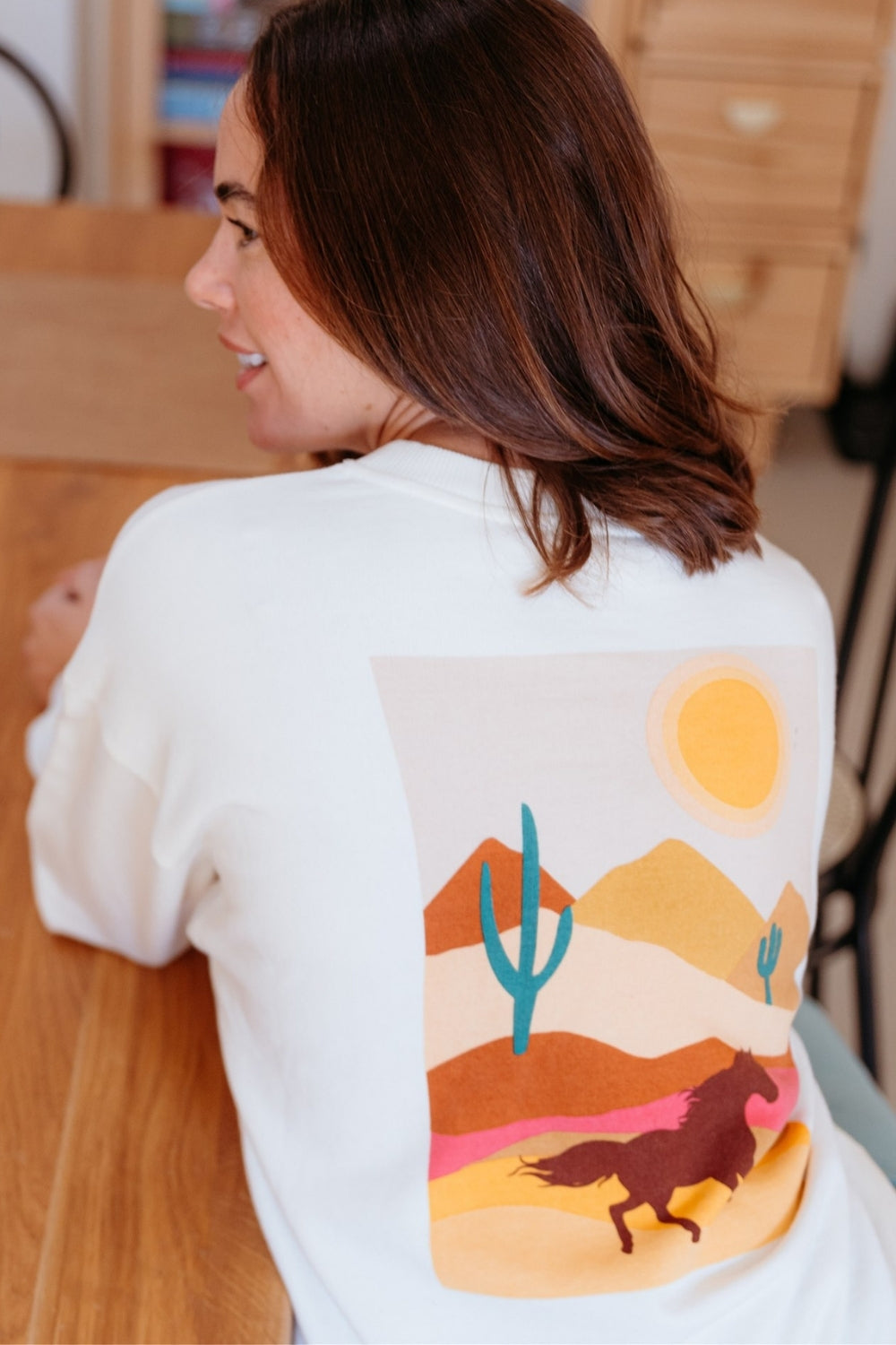 Person wearing a white sweatshirt with a desert landscape graphic on the back.