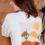 Person wearing a white sweatshirt with a desert landscape graphic on the back.