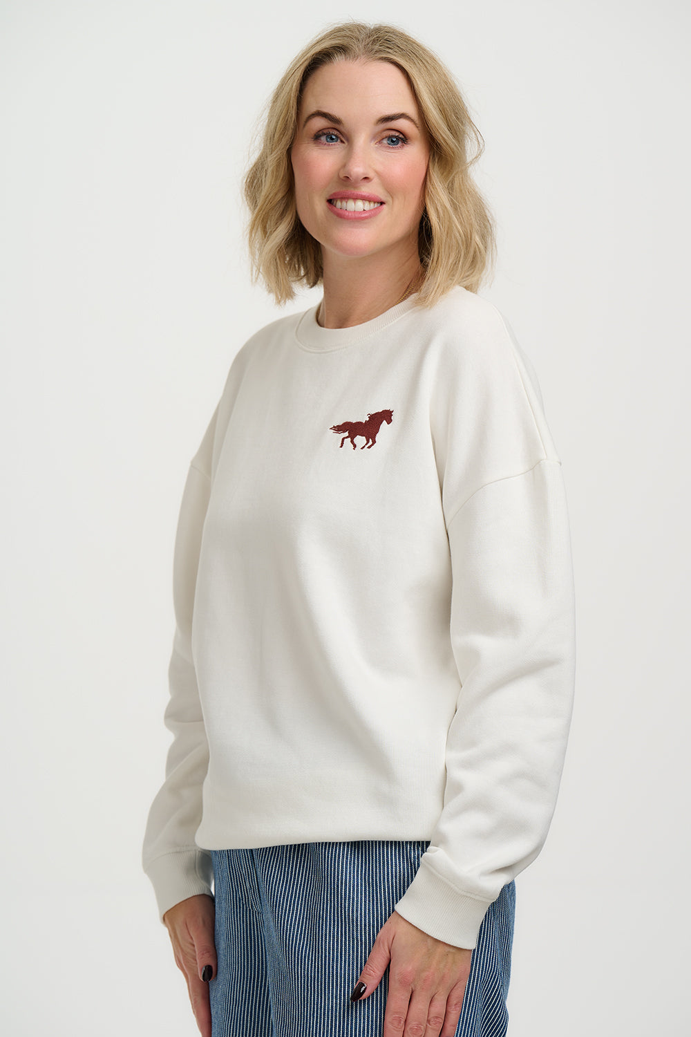 Woman wearing a white sweater with a red horse emblem on a plain background