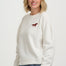 Woman wearing a white sweater with a red horse emblem on a plain background