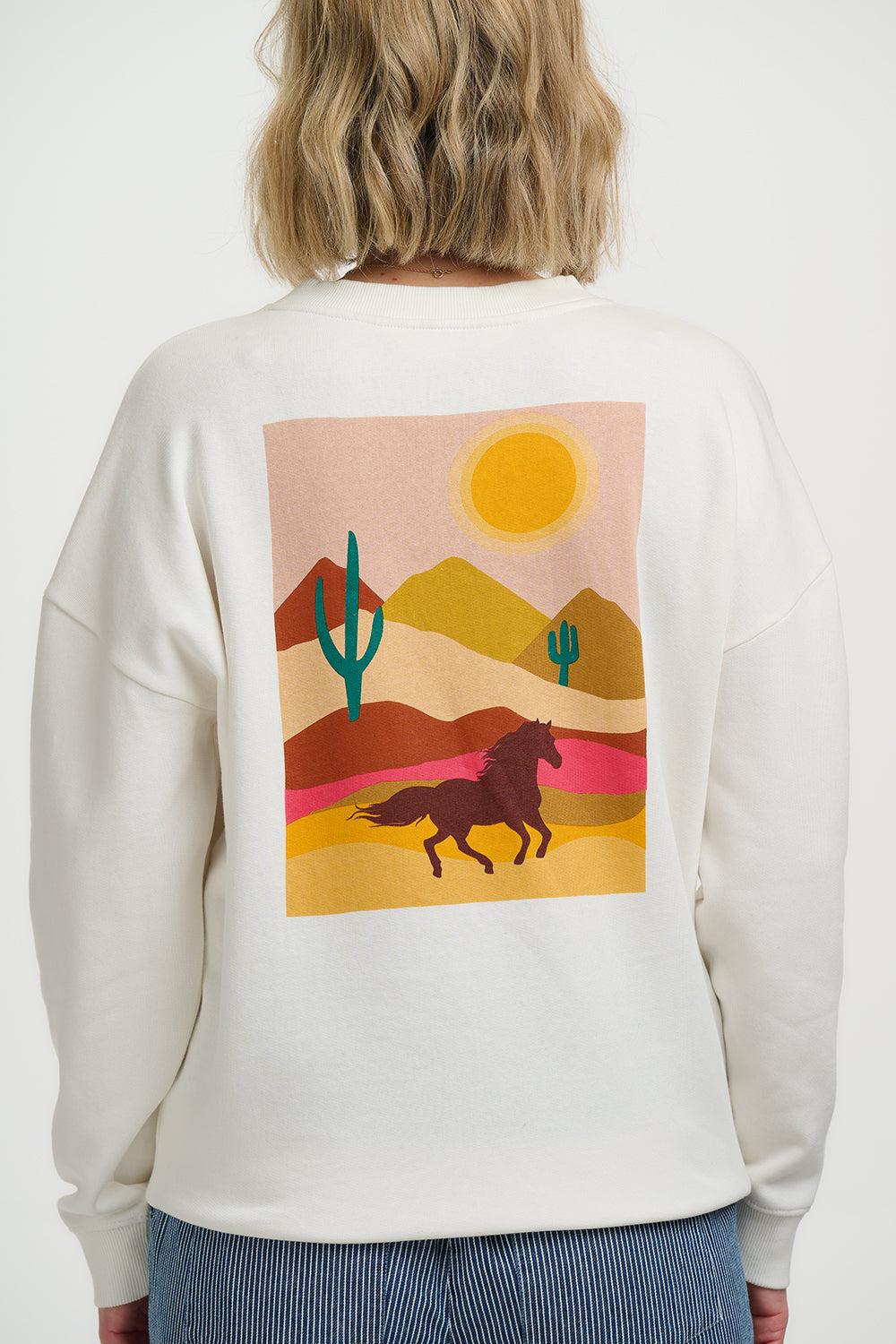 Person wearing a white sweatshirt with a desert landscape graphic on the back.