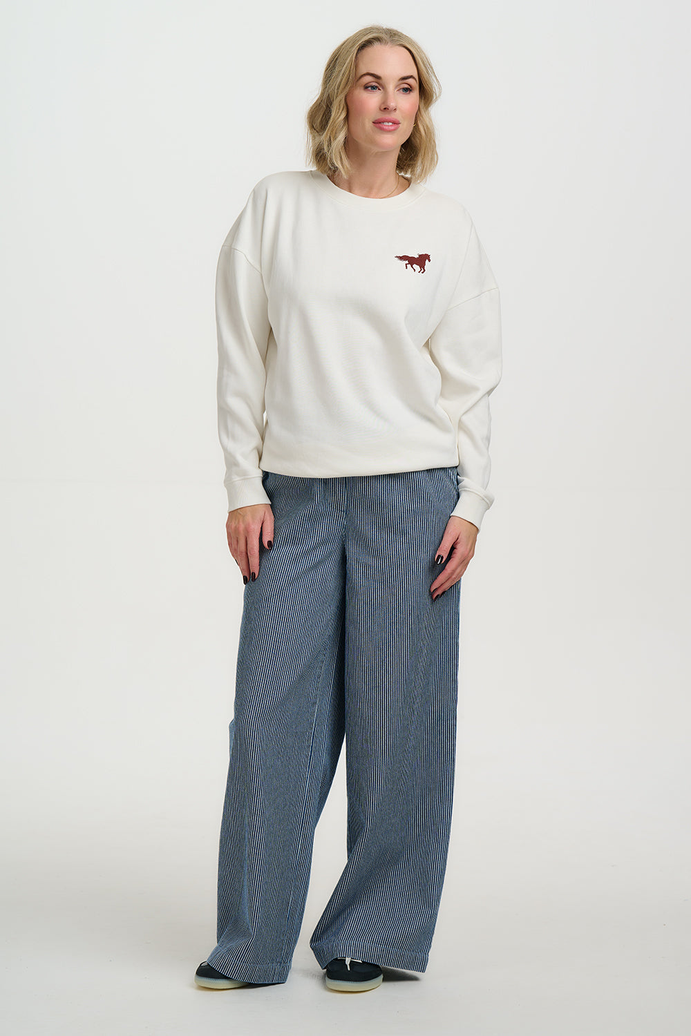 Woman wearing a white sweater with a red logo and blue pants on a white background