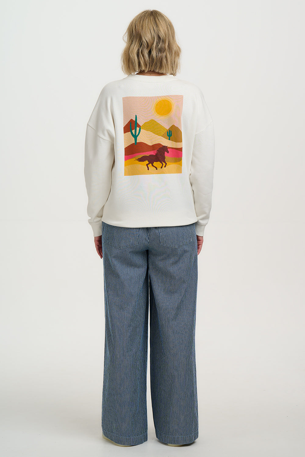 Person wearing a white sweatshirt with a desert scene graphic on the back, standing against a plain background.