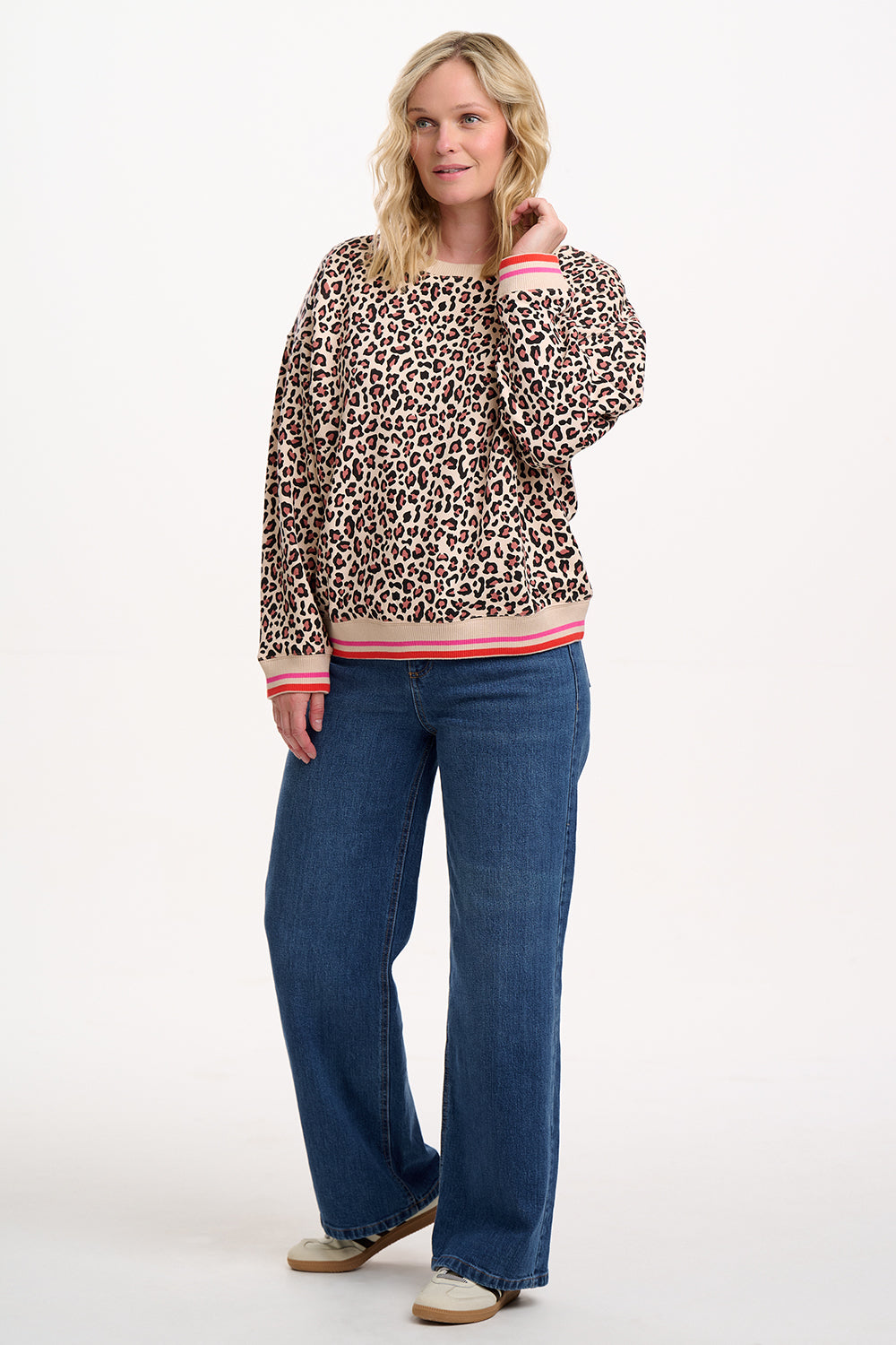 Sugarhill Brighton model wearing a leopard print sweater and blue jeans on a white background