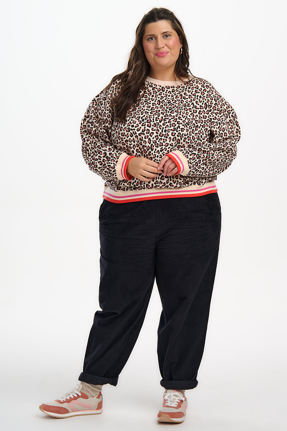 Person wearing a leopard print sweater with pink trim and black pants on a white background