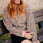 Sugarhill Brighton model wearing a leopard print shirt and gray beanie sitting on a bench.
