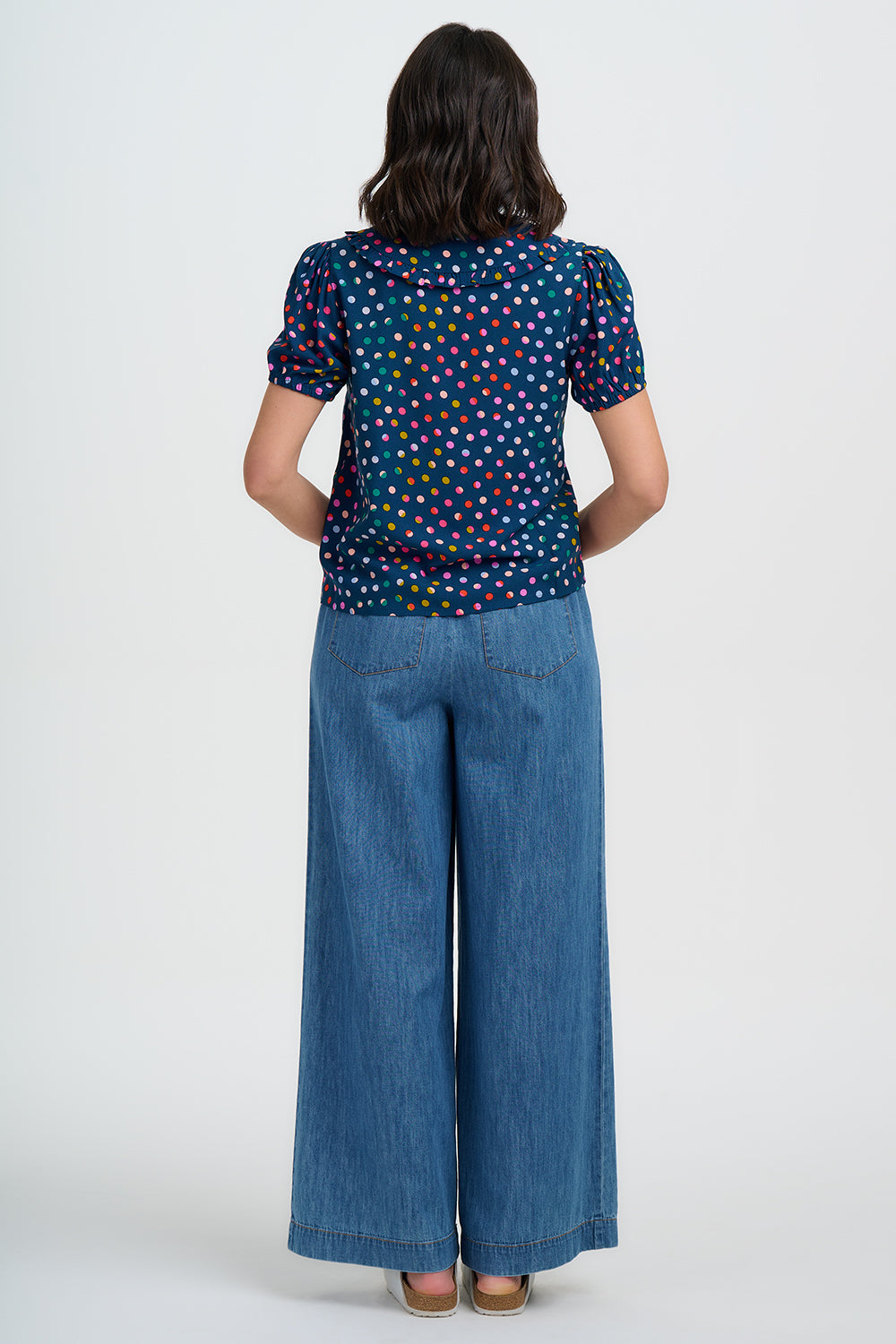Person wearing a patterned top and blue jeans on a white background