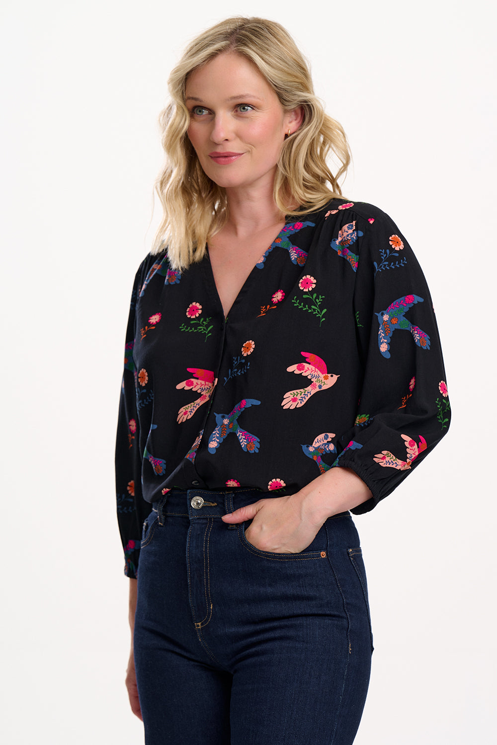 Sugarhill Brighton model wearing a black blouse with colourful floral embroidery on a white background