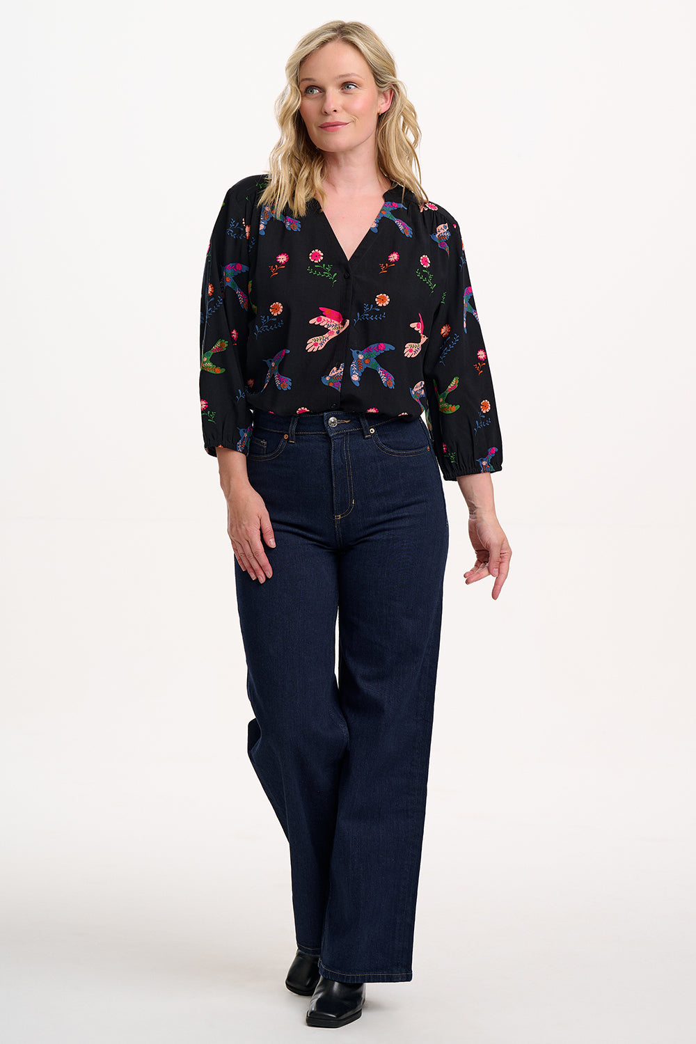 Sugarhill brighton model wearing a black floral blouse and navy jeans on a white background