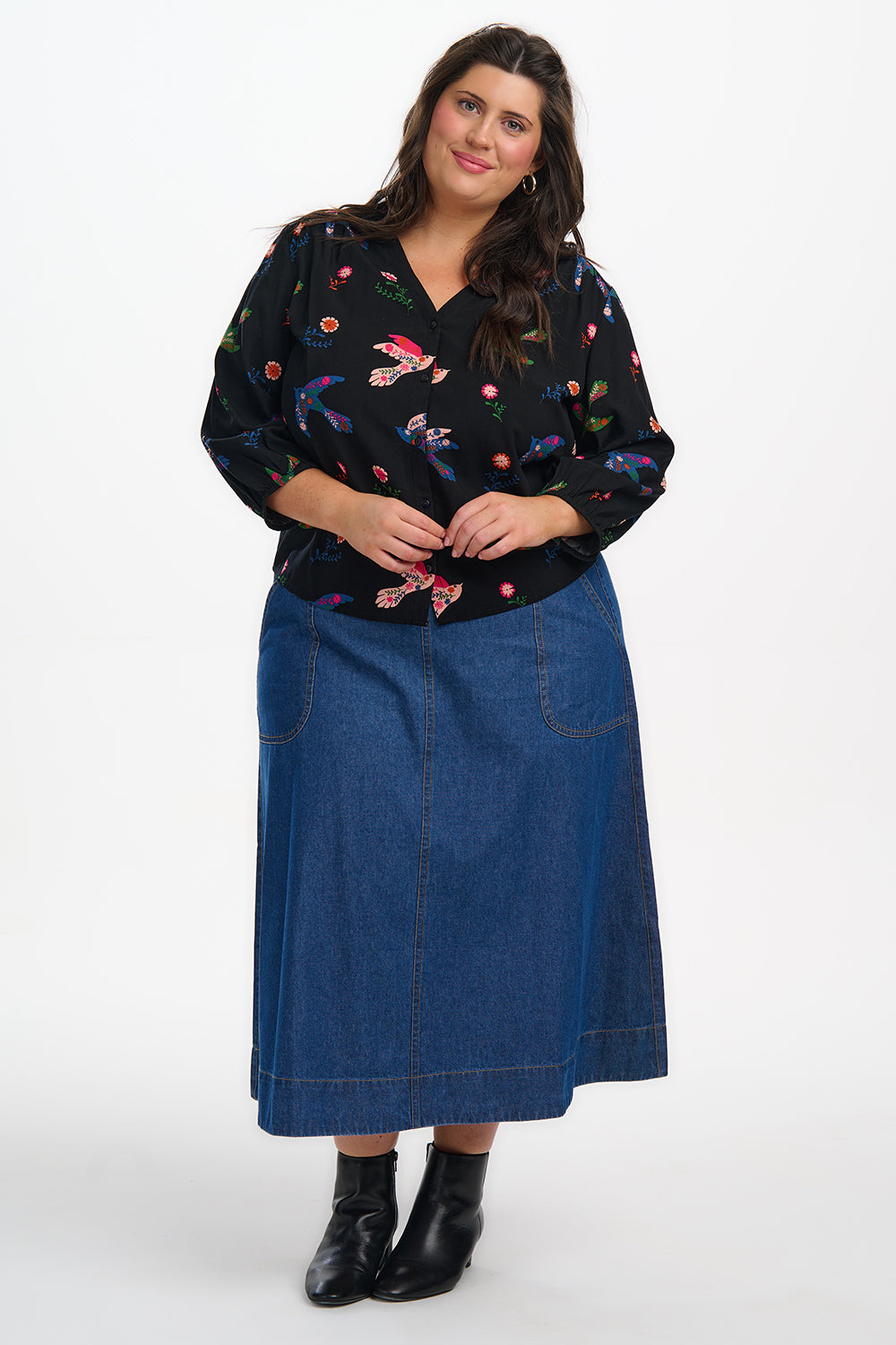 Woman wearing a black floral blouse and blue denim skirt on a white background