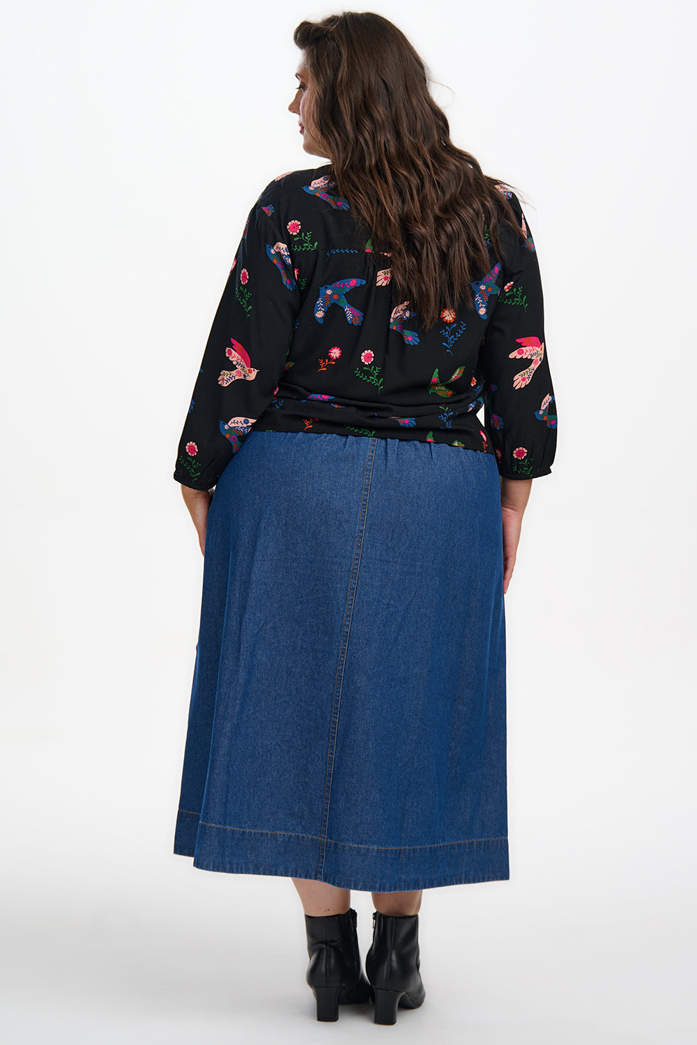 Person wearing a black floral blouse and blue denim skirt on a white background