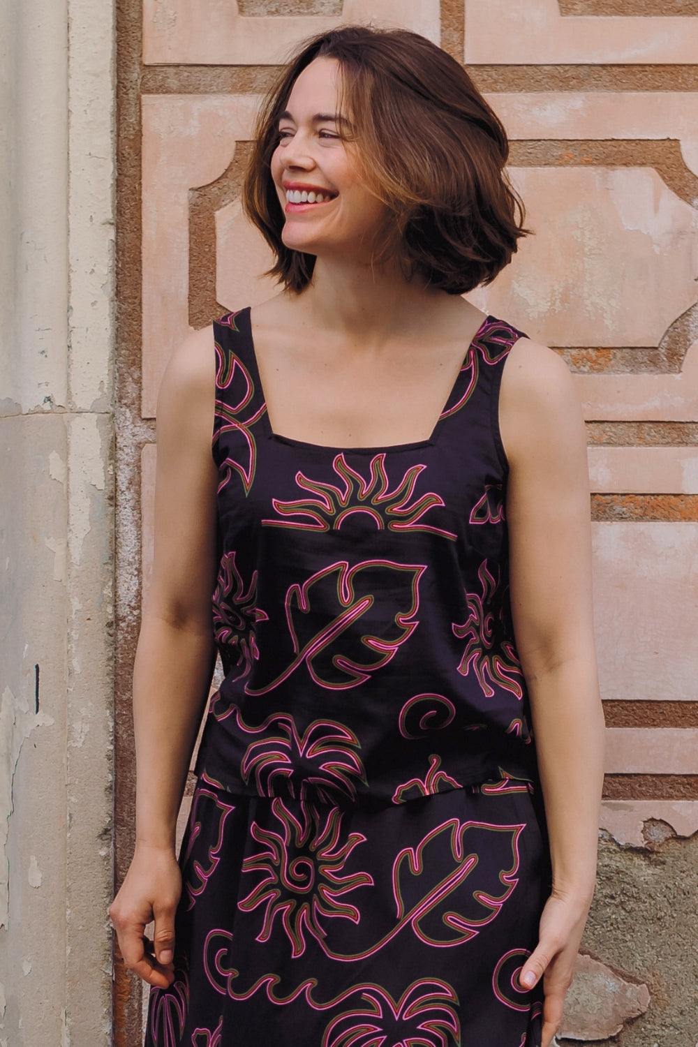 Woman wearing a black dress with pink floral patterns against a stone wall.