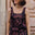 Woman wearing a black dress with pink floral patterns against a stone wall.