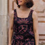 Woman wearing a black dress with pink floral patterns against a stone wall.