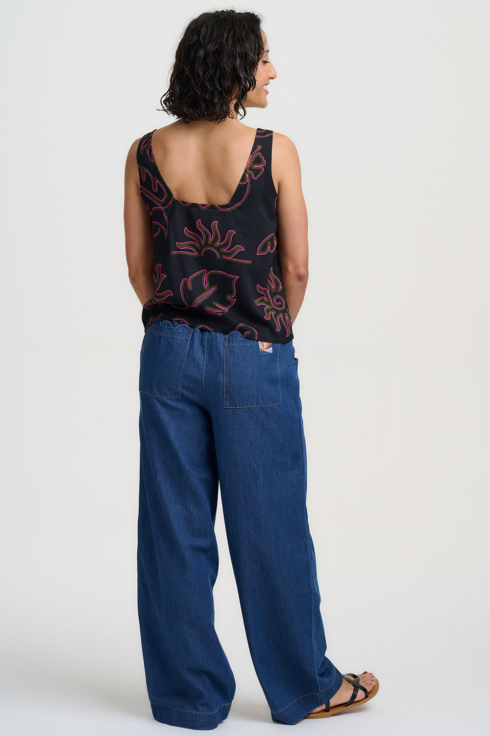 Woman wearing a black tank top with red patterns and blue pants on a white background