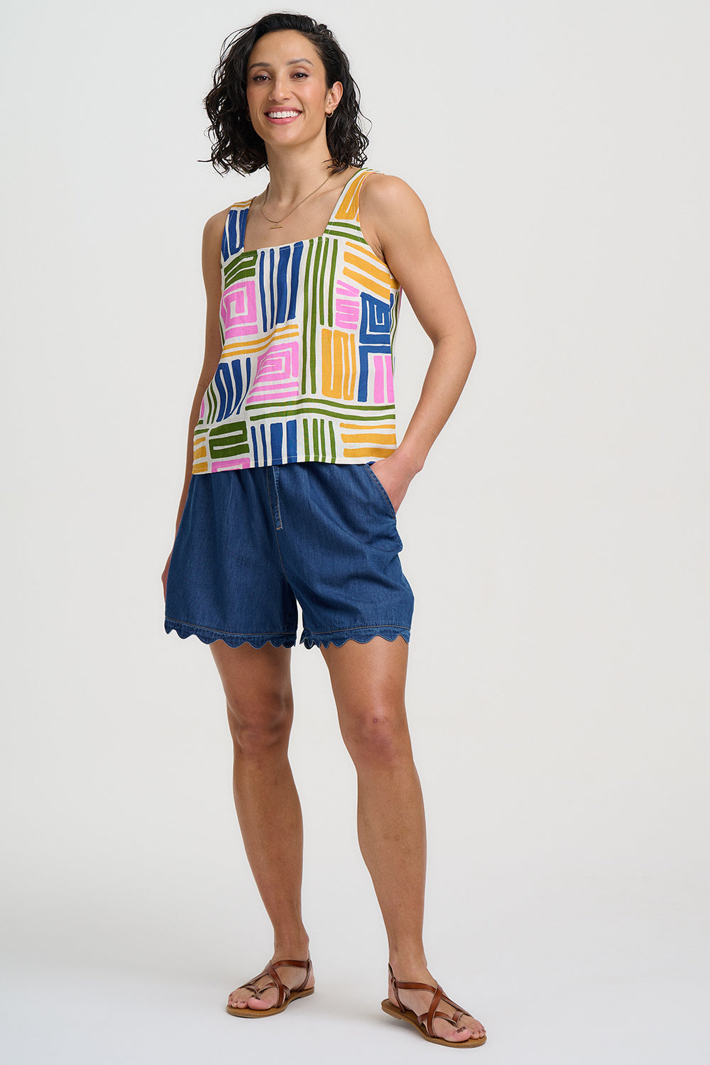 Woman wearing a colorful tank top and blue shorts on a white background