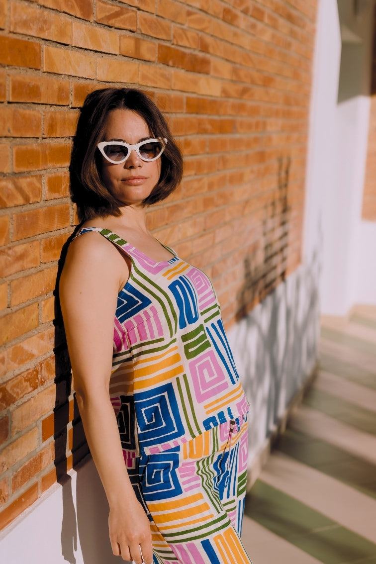 Woman in a colorful geometric dress standing against a brick wall.