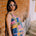 Woman in a colorful geometric dress standing against a brick wall.