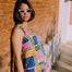 Woman in a colorful geometric dress standing against a brick wall.