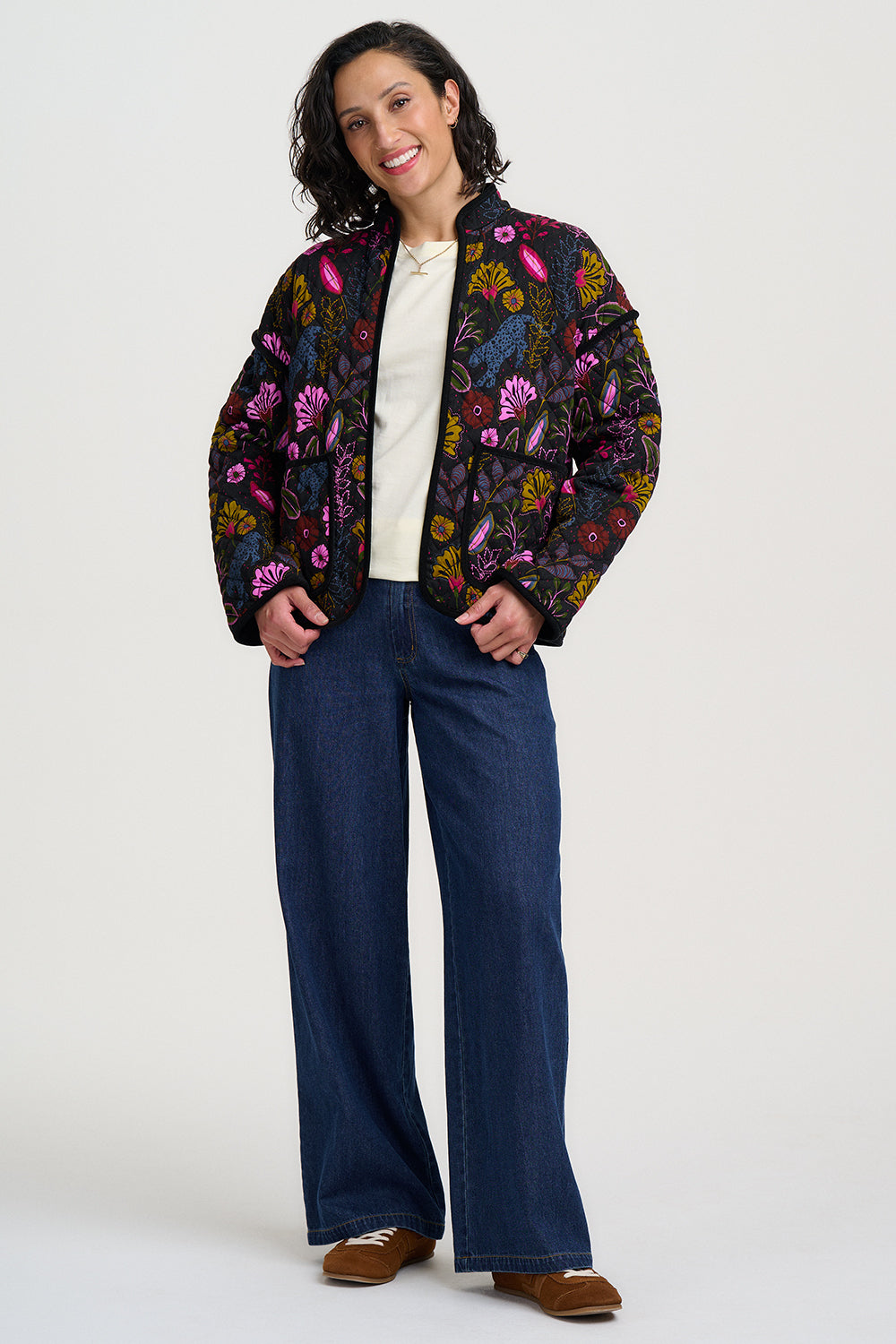 Woman wearing a colorful floral jacket and blue jeans on a white background