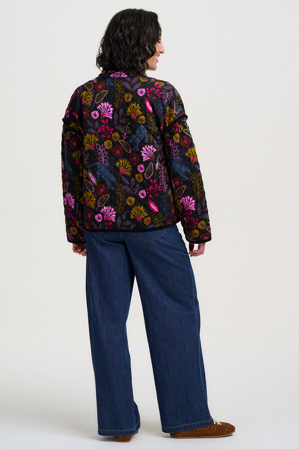 Person wearing a colorful floral jacket and blue jeans on a white background