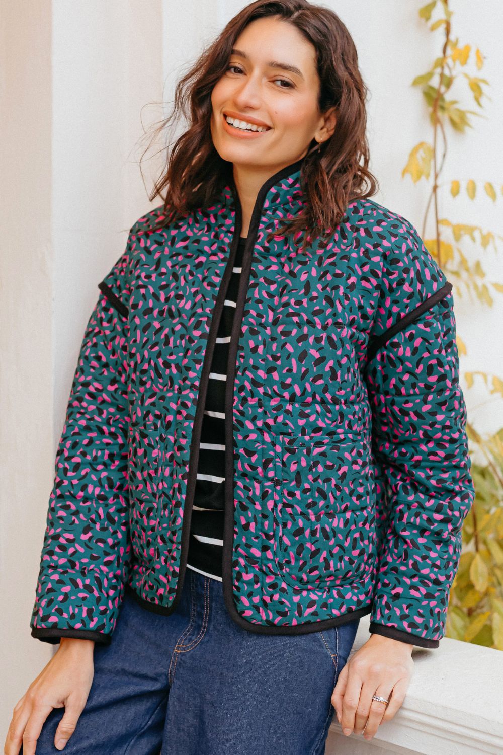 Woman wearing a patterned jacket standing against a neutral wall with decorative elements.