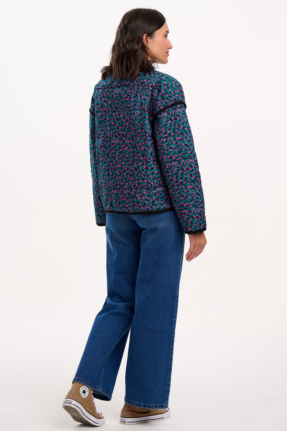 Person wearing a patterned jacket and blue jeans on a white background