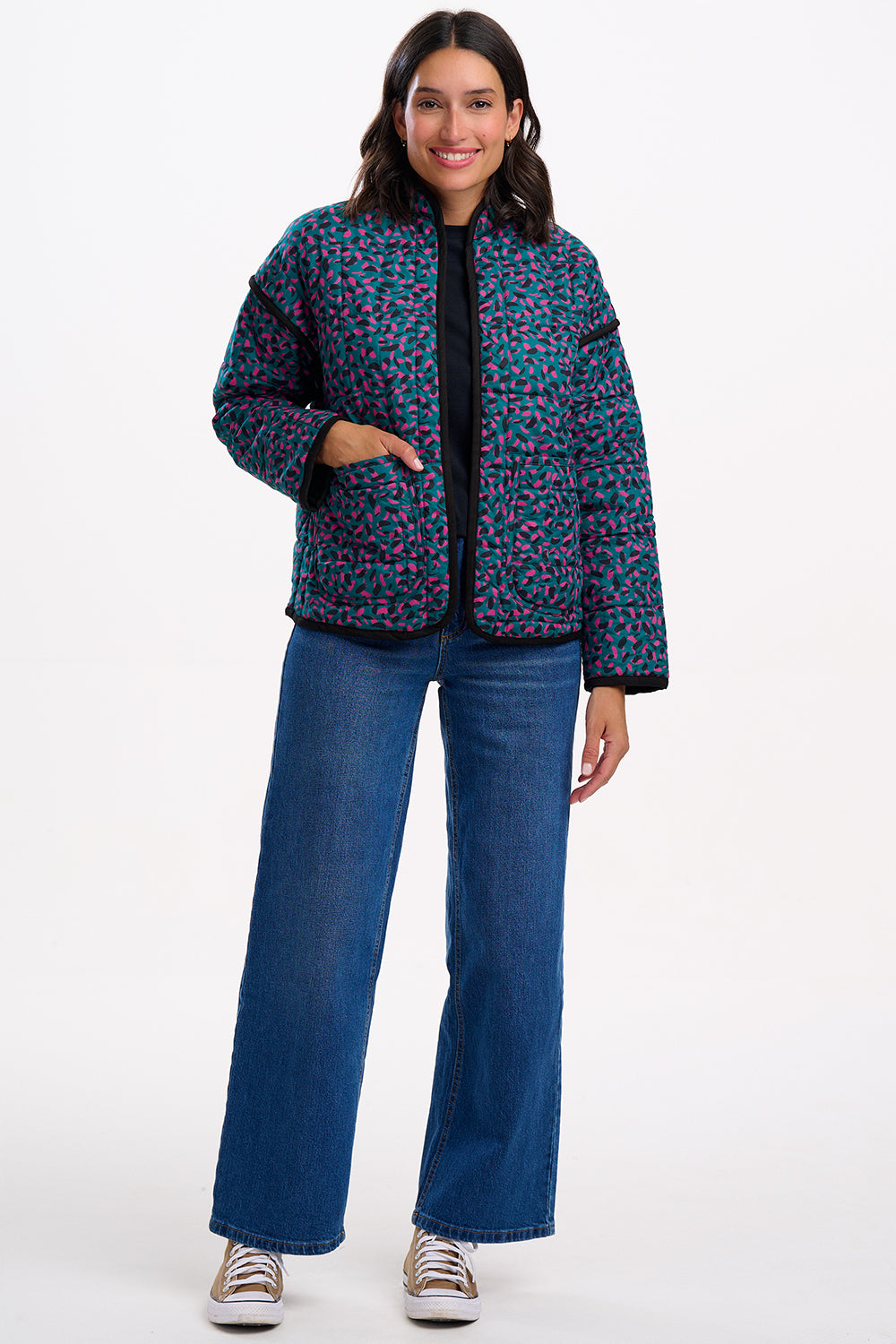 Woman wearing a patterned jacket and blue jeans on a white background