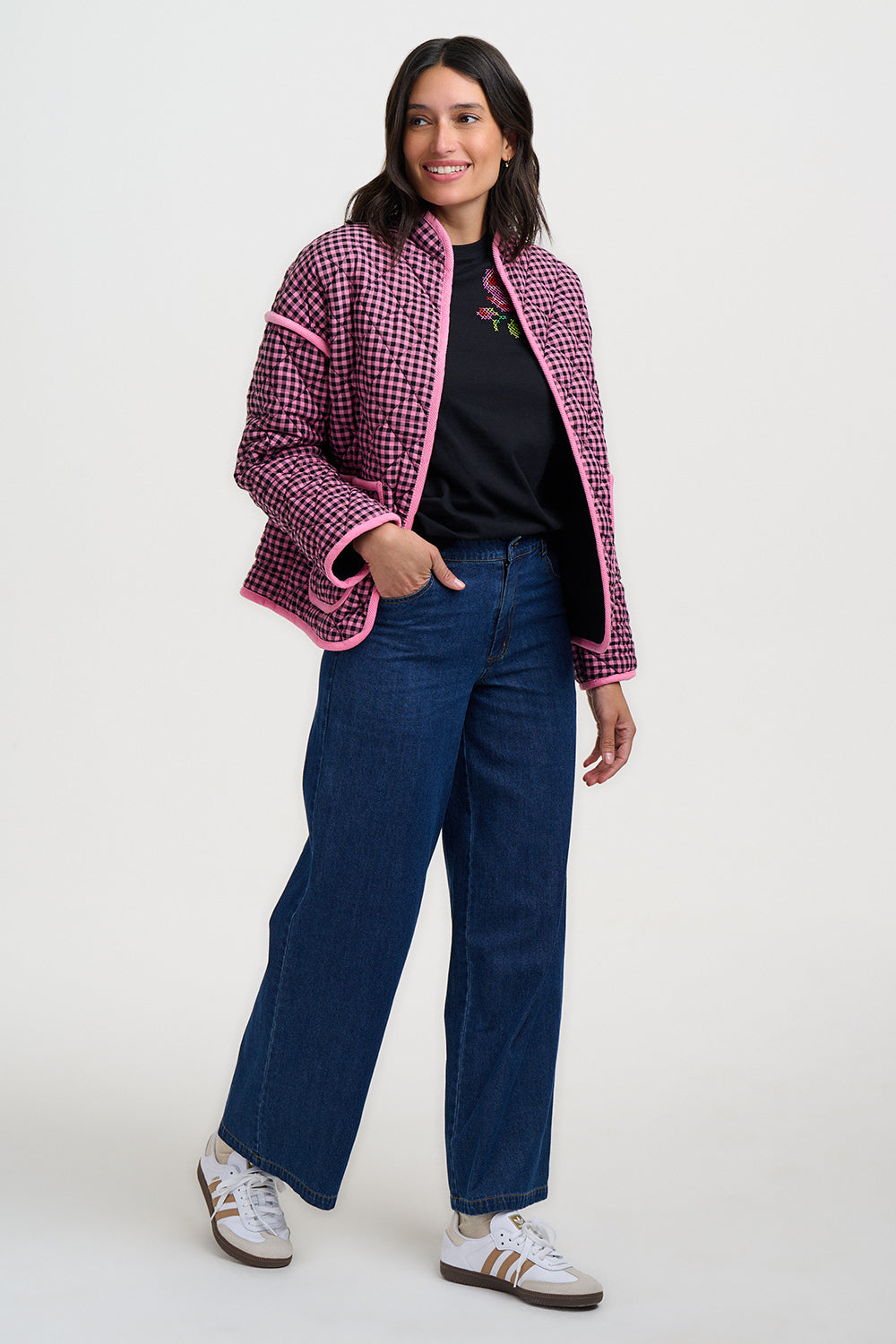 Woman wearing a pink and black checkered jacket with blue pants on a white background