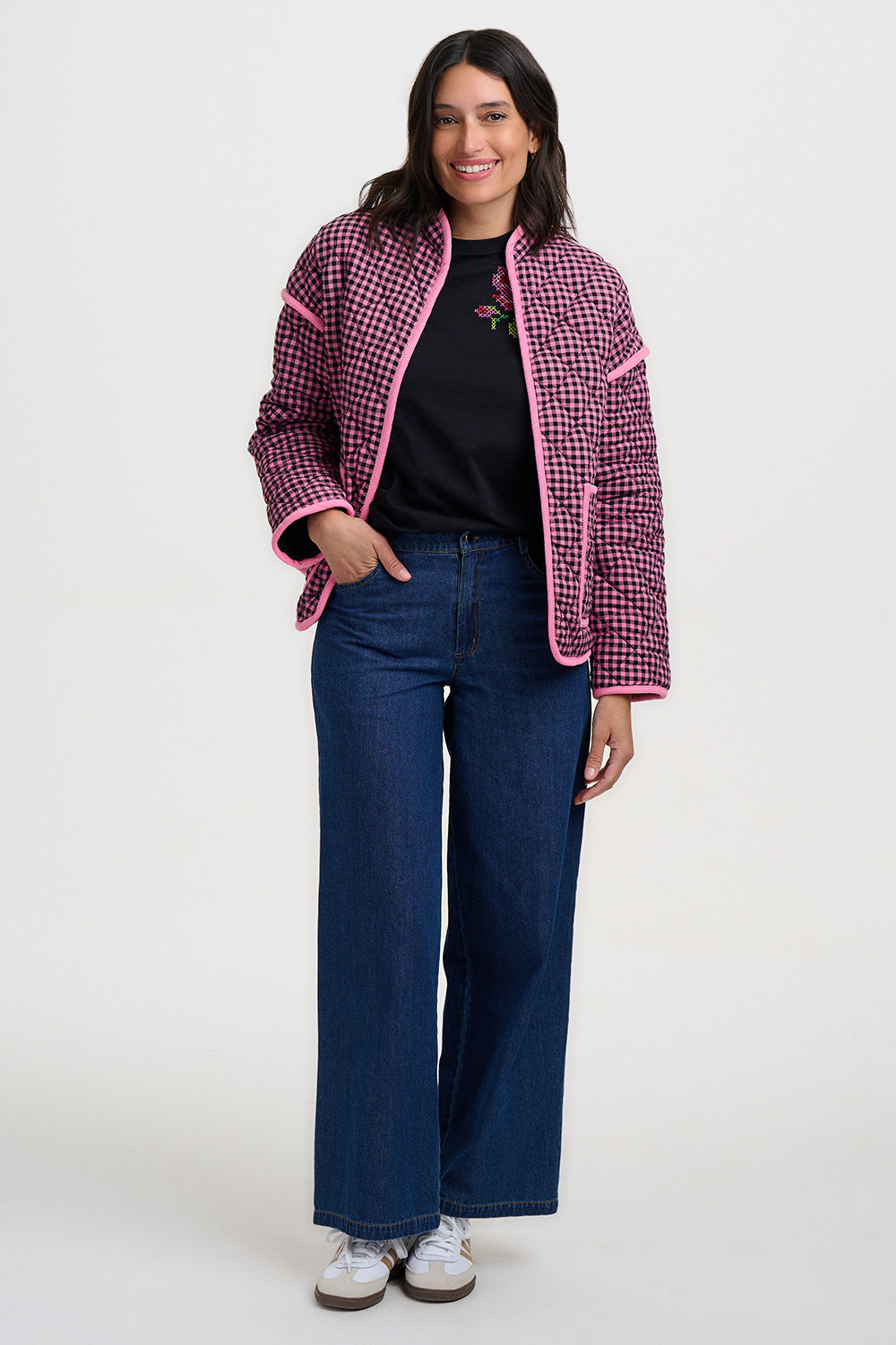 Woman wearing a pink and black checkered jacket with blue jeans on a white background