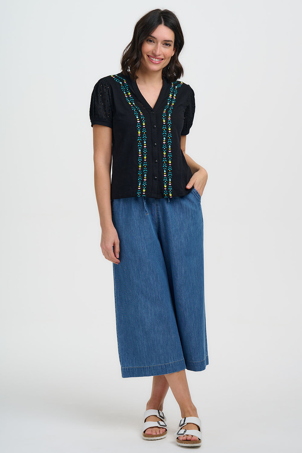 Woman wearing a black top with embroidery and blue denim pants on a white background