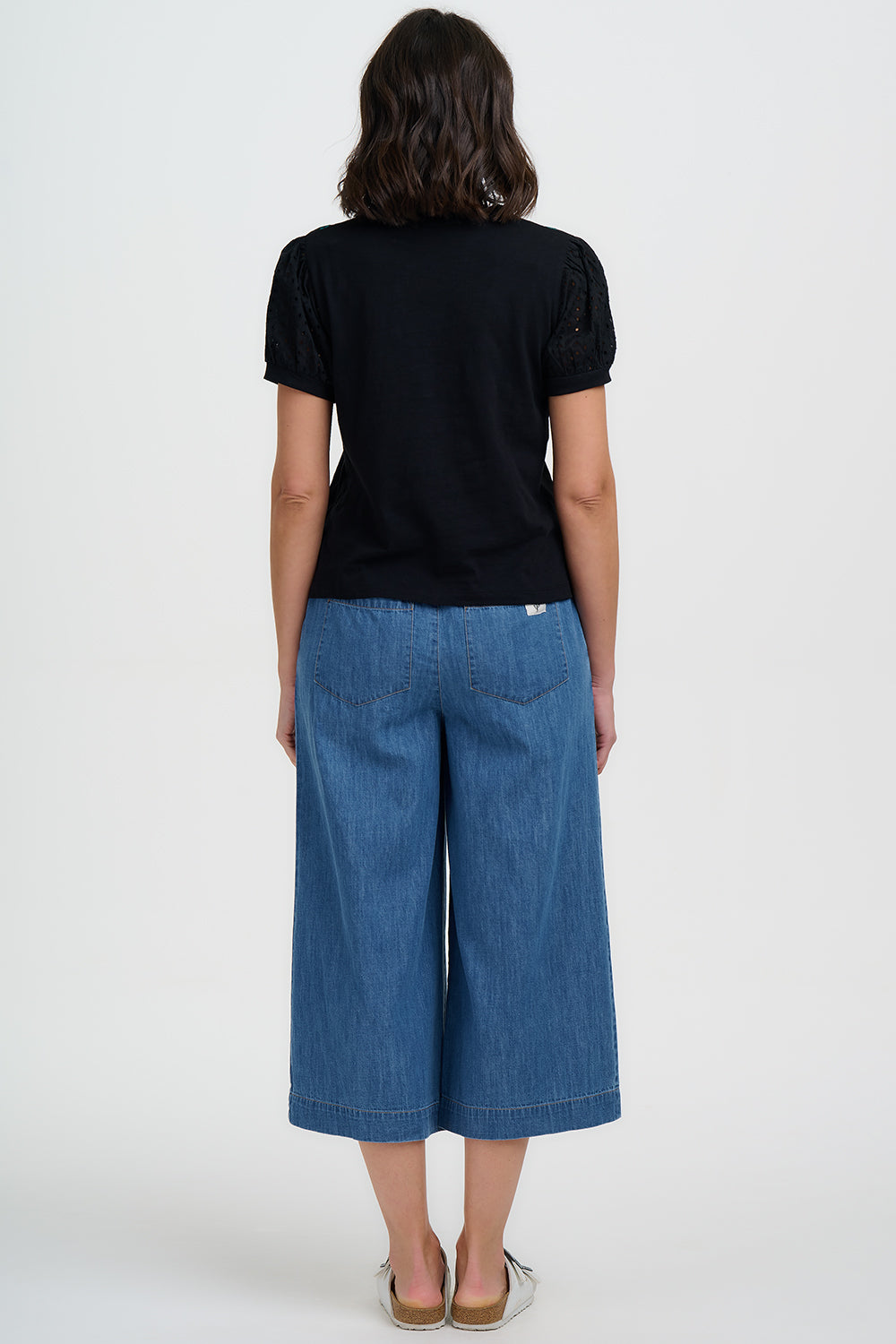 Person wearing a black t-shirt and blue denim pants on a white background