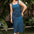 Woman wearing a blue polka dot dress standing outdoors with greenery in the background
