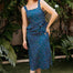 Woman wearing a blue polka dot dress standing outdoors with greenery in the background