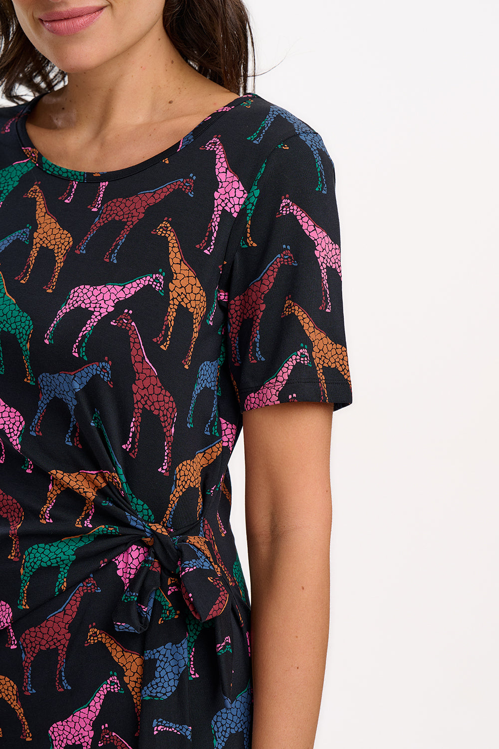 A woman wearing a midi jersey dress with a giraffe print in multiple colors on a black base.