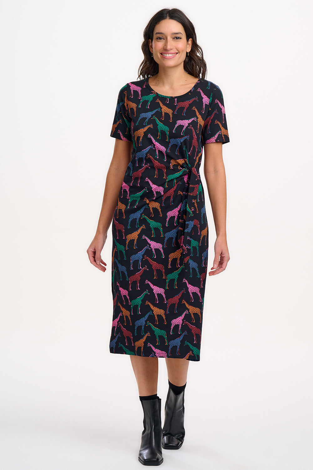 A woman wearing a midi jersey dress with a giraffe print in multiple colors on a black base.
