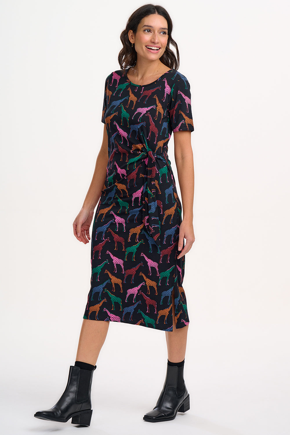 A woman wearing a midi jersey dress with a giraffe print in multiple colors on a black base.