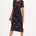 A woman wearing a midi jersey dress with a giraffe print in multiple colors on a black base.