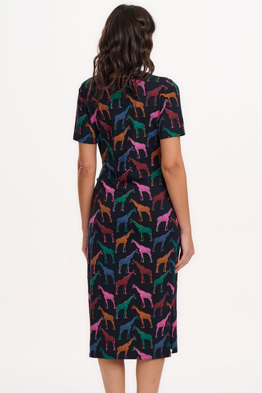 A woman wearing a midi jersey dress with a giraffe print in multiple colors on a black base.