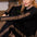 A woman with red hair sits on a brown couch wearing a black long-sleeve pajama set with leopard print stripes on the sleeves and legs.
